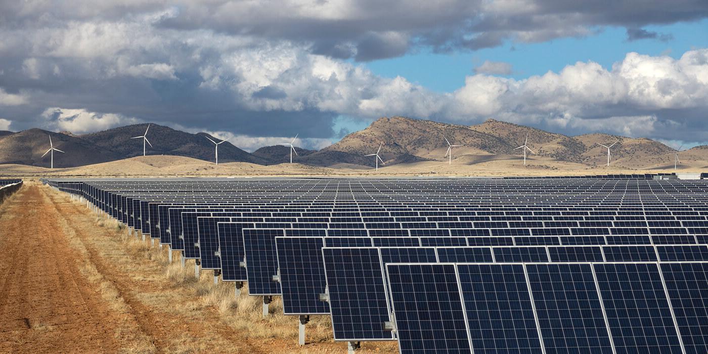 photo of solar panels and windmills against mountain background with blue sky