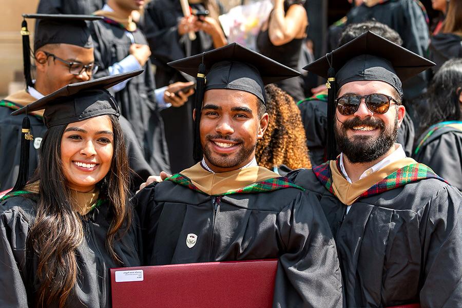 Three students at MBA commencement in cap and gown.