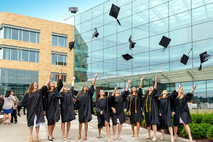 Group of female students throw their graduation caps in the air in front of the Tepper building.